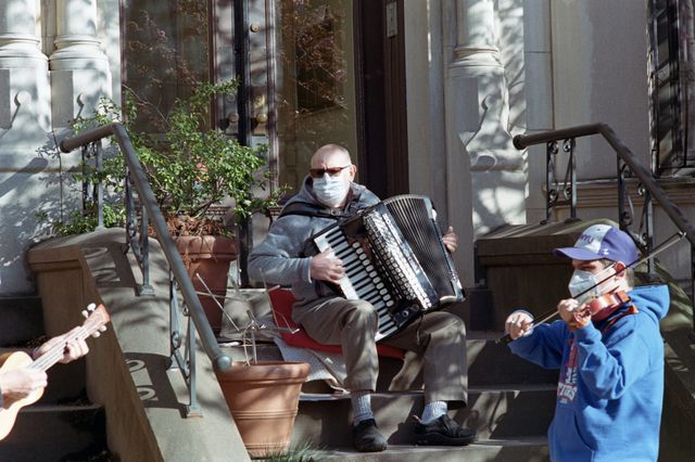 A photo of people playing music in masks on their stoop